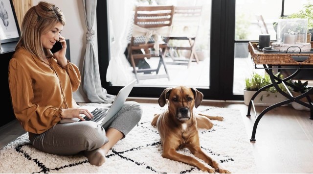 Woman sitting on the floor with a laptop with a phone to her ear.