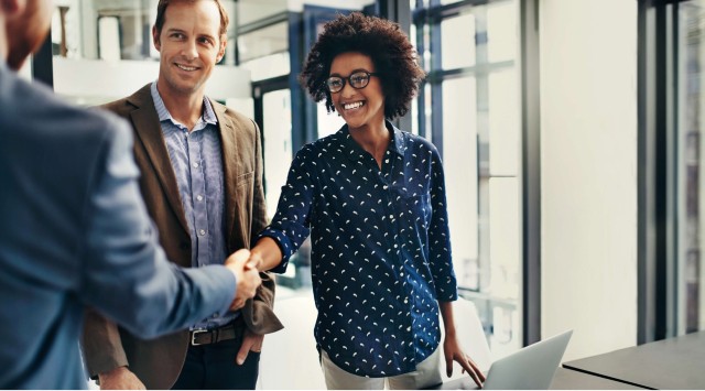young woman shaking hands with a man, another man stands beside her