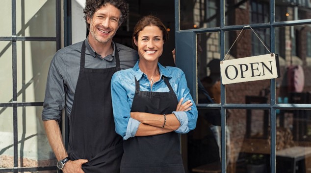 Business owners standing next to their business with an open sign hanging on the door