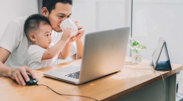man drinking coffee with a toddler in his lap while working on a laptop