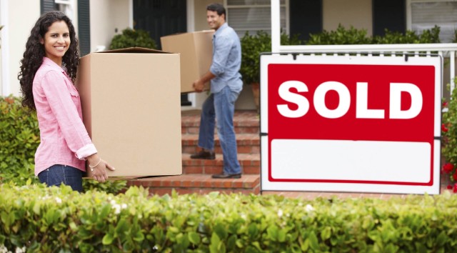 couple carrying boxes into a house with a sold sign in front