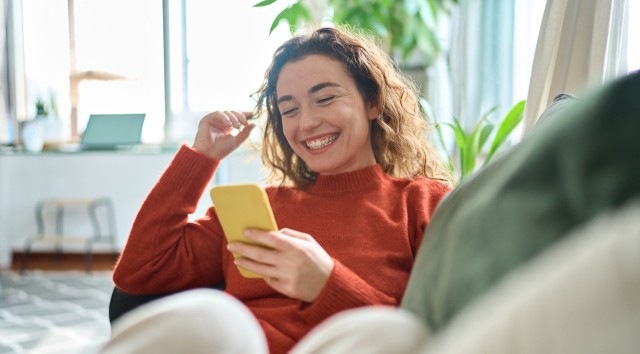 woman laying on sofa looking at phone and smiling