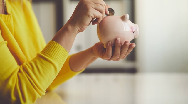 close-up of a woman holding a piggy bank and putting a coin in