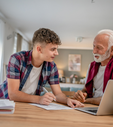 teenage boy and senior man sitting at a table with papers and a laptop