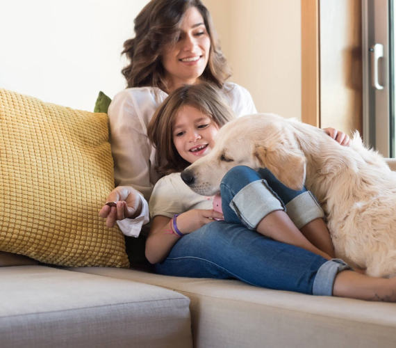 a woman, girl, and dog piled up together on a sofa